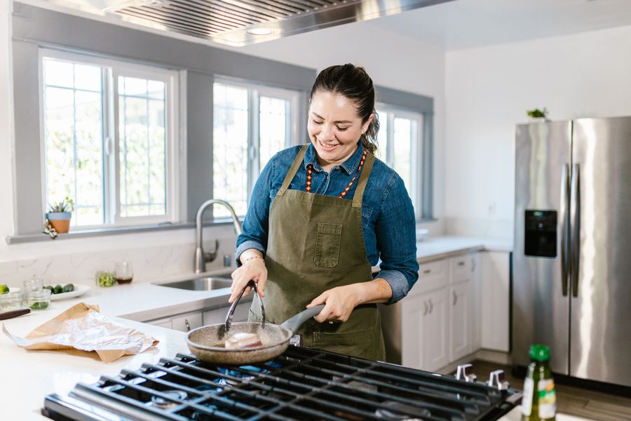 Professional household cook in a cozy kitchen cooking food in a frying pan
